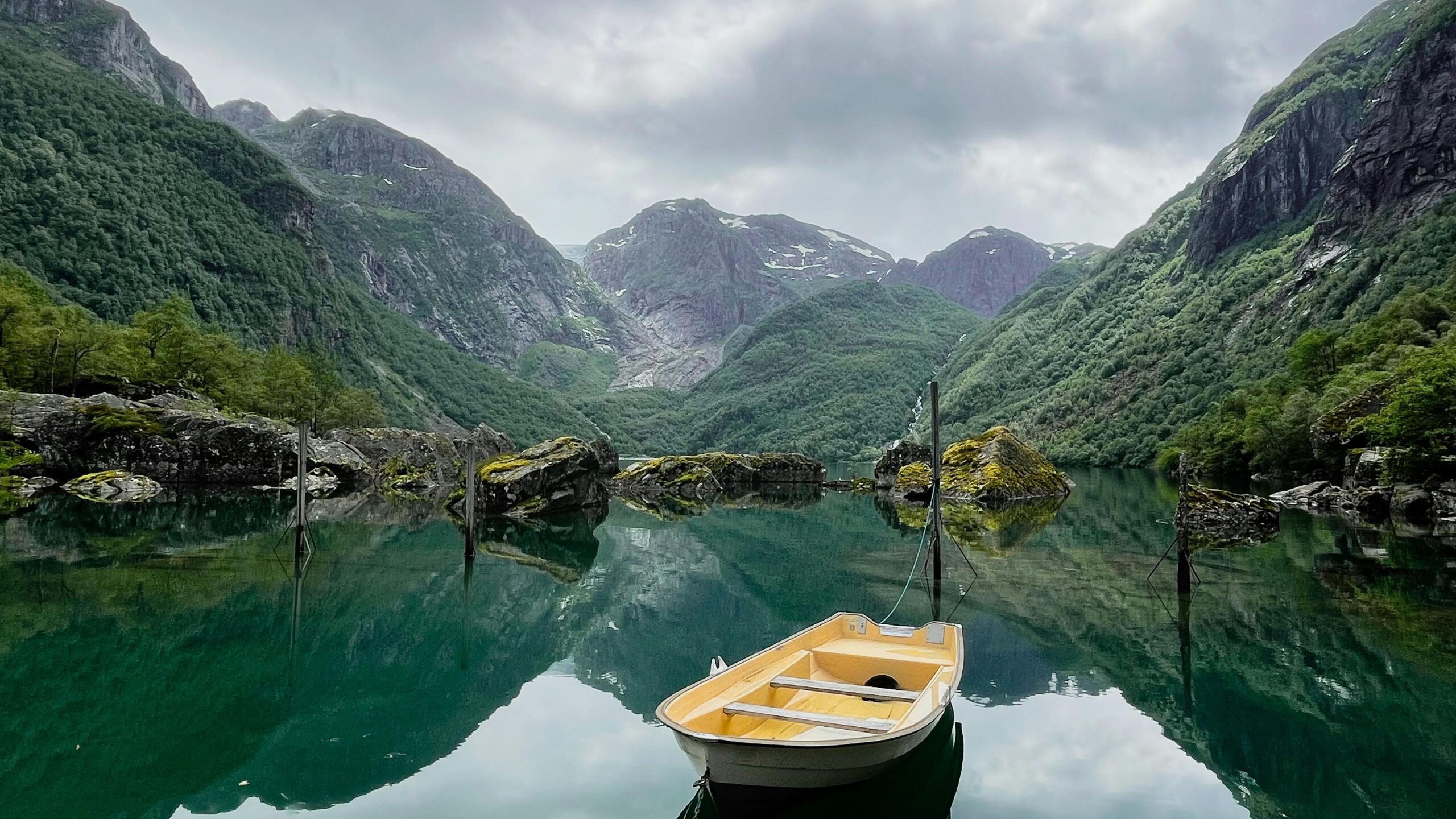 Peaceful lake with a yellow boat surrounded by lush green mountains under a cloudy sky